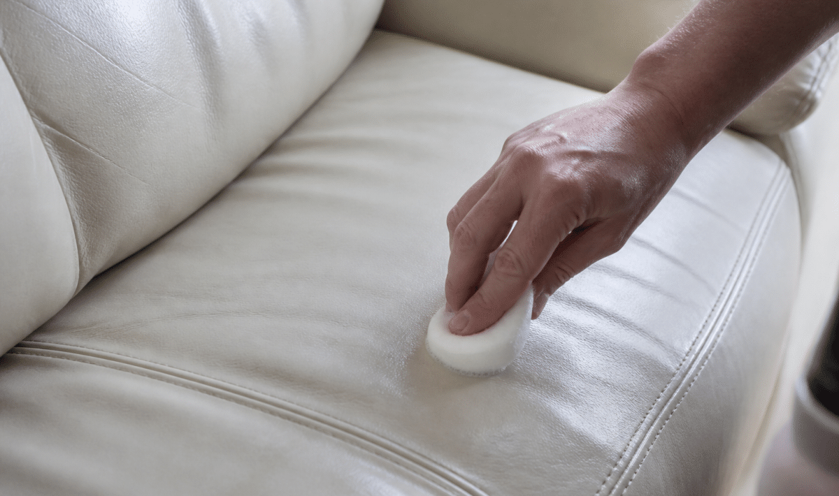 Main appliquant produit nettoyant sur coussin cuir blanc