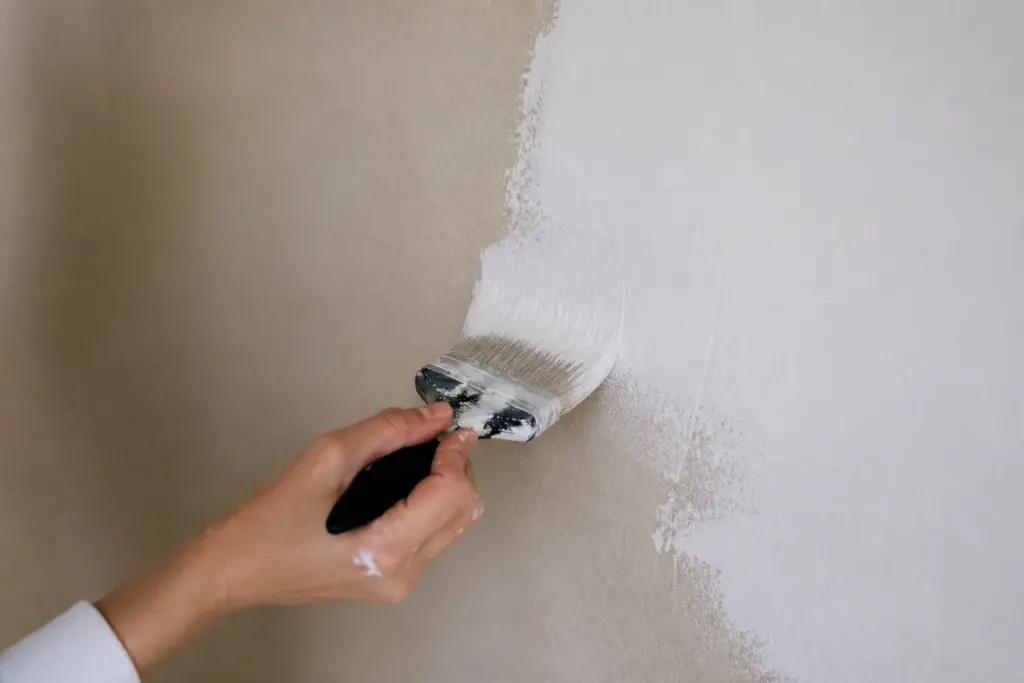 Brosse appliquant peinture blanche sur mur beige
