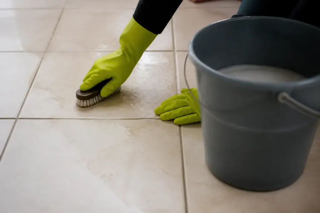 Mains gantées frottant des carreaux beige avec un seau